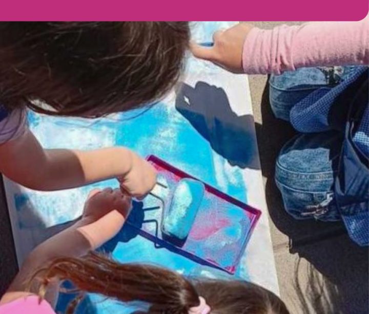 estudiantes pintando una lámina juntas con rodillo y pintura azul.